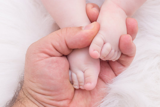 Baby feet on his father hands in soft white blanket 