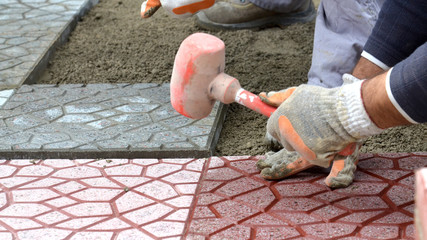 Hands of a builder laying new paving stones carefully placing one in position on a leveled and...