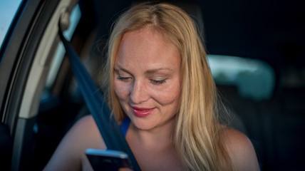 Plakat Attractive blonde girl uses smartphone in the car