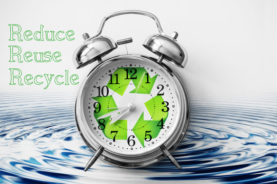 Alarm clock with the green recycle symbol on it. Pure water in the background and the words "Reduce", "Reuse" and "Recycle" written near the clock on white background
