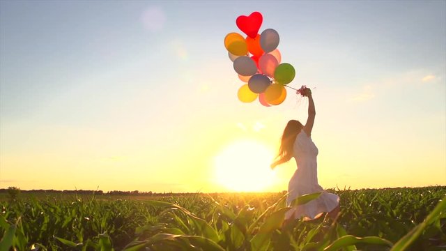 Beauty girl running on summer field with colorful balloons over clear blue sky. Slow motion 240 fps. 4K UHD video 3840X2160