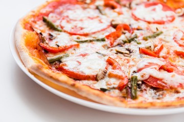 Pizza with tomato, mushrooms, bell peppers on a white plate on a light background