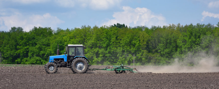 A blue tractor plows the field in the spring