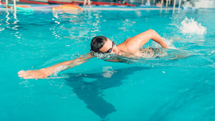 Swimmer in glasses swims in indoor swimming pool