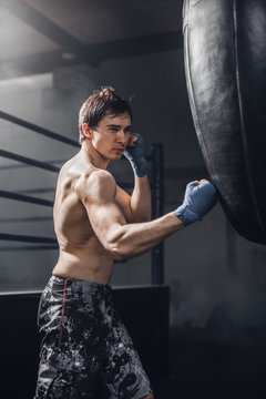 Muscular fighter prepare for practicing some kicks with punching bag. Muscular strong man on background boxing gym.
