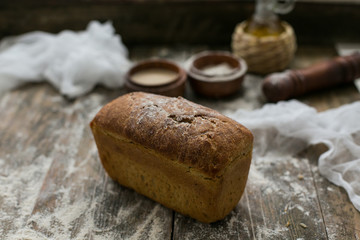 Close up view of fresh brown crispy loaf of bread lying on the wooden table sprinkled with flour