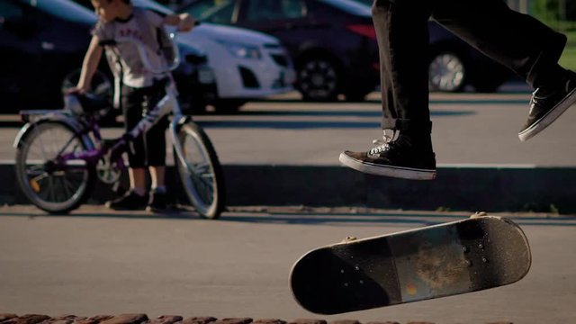 Close up shot of the feet of an adult teenager who performs a jump on a big fanbox in a self-made skatepark, then people land badly