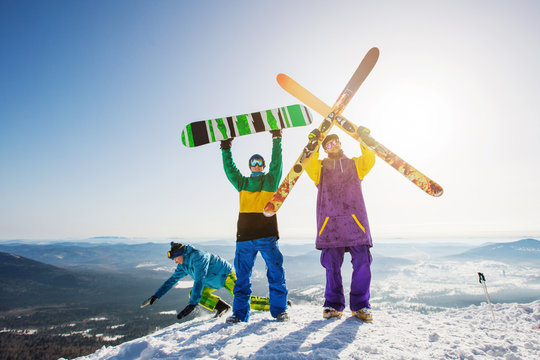 Happy Skier and snowboarder friends standing on mountain top with ski and snowboard in hands