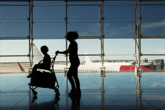 Silhouette of woman carrying wheelchair with child and suitcase at the airport