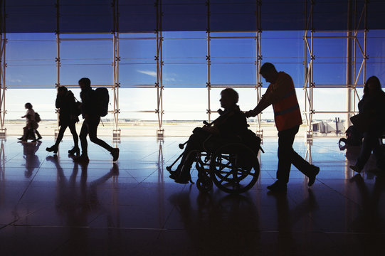 Silhouette of  man in wheelchair and people carrying luggage and walking in  airport