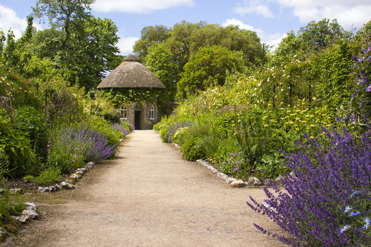 The 19th Century thatched round house surrounded by beautiful flower beds and gravel paths in the walled garden at West Dean gardens in Hampshire, England 