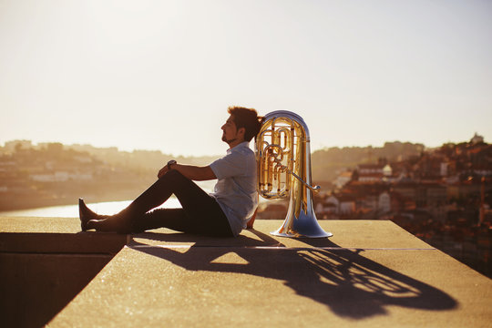 Street musician sitting with tuba outdoor at sunset. Europe city background