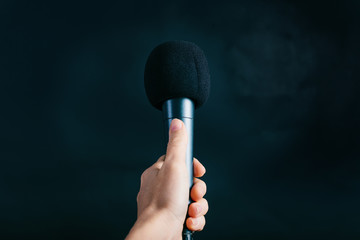 Female hand holding microphone on black background
