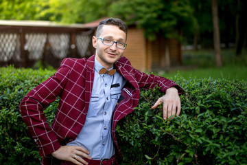 Portrait of a stylish young man wearing glasses plaid suit and a wooden bow tie. The man is smiling