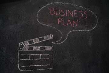 Open movie clapper and speech bubble with business plan writing drawn with chalk on blackboard