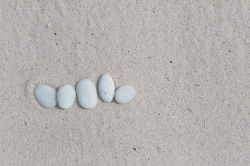 Fototapeta na wymiar White pebbles, round small stones in a row on dry white sand beach, space for letters or text
