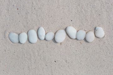 White pebbles, round small stones in a row on dry white sand beach, space for letters or text