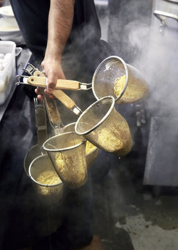 Man holding colanders filled with noodles in restaurant kitchen
