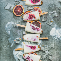 Healthy summer dessert. Blood orange, yogurt and granola popsicles on ice cubes over grey concrete background, top view, square crop. Clean eating, dieting, weight loss concept