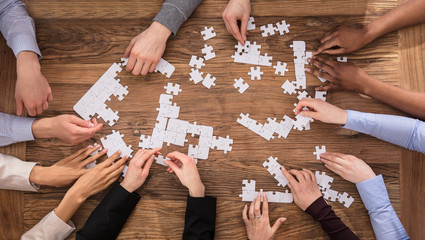 High Angle View Of Businesspeople Solving Jigsaw Puzzle - obrazy, fototapety, plakaty
