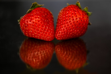 Red strawberries on black glossy background with reflection