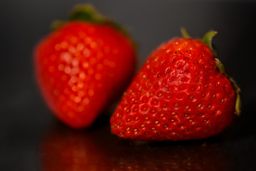 Red strawberries on black glossy background with reflection