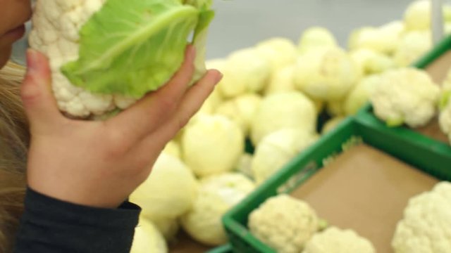 Girl in supermarket selects cauliflower, close-up. Female customer shopping for vegetables in supermarket.