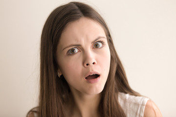 Headshot portrait of confused young woman. Beautiful teen girl with shocked facial expression looking at camera with surprise. Lovely lady feeling resentment, misunderstanding. Close up. Front view