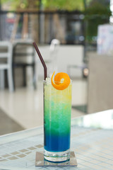 A glass of Iced mixed blue hawaii soda with lemonade, orange juice and honey on table and on blurred background, Colorful Cocktail or Tropical Mocktail.