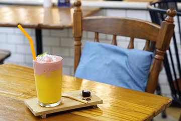 A glass of fresh fruit smoothie with milk, made from mango and strawberry topped with mint leaves on wooden table.