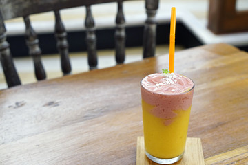 A glass of fresh fruit smoothie with milk, made from mango and strawberry topped with mint leaves on wooden table.