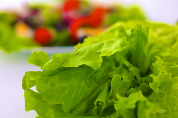 fresh raw vegetable salad with tomatoes and green lettuce on wooden plate isolated over white background
