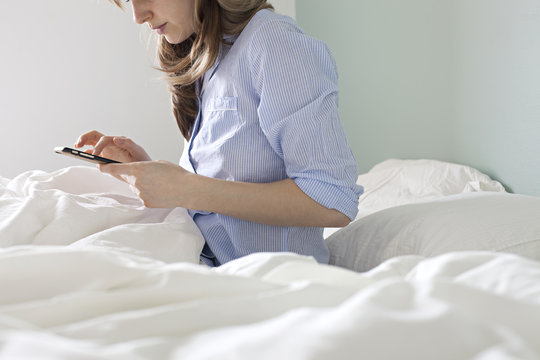Brownhaired girl checking her phone from bed in pyjamas