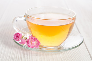 Glass cup of tea with rose on white wooden table