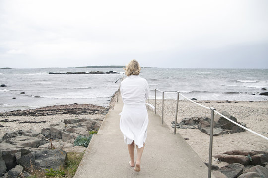 Rear view of woman wearing white bathrobe walking on pier