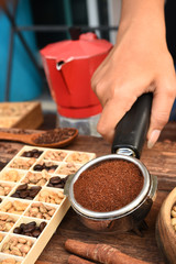 Freshly ground coffee beans in a metal filter and coffee beans in bowl with red kettle on the side.