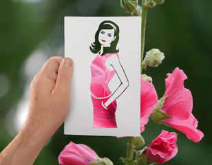 A hand holds a paper stencil of young long-haired girl against background of pink flowers