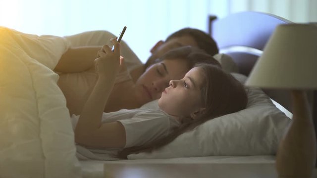 The girl phone on the bed near parents