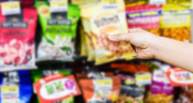 hand of woman choosing or taking sweet products, snacks on shelves in convenience store
