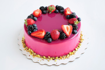 Birthday mousse cake with pink mirror glaze and with berries, pistachios. Picture for a menu or a confectionery catalog.