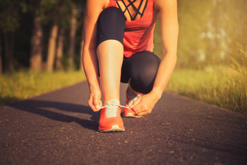 Frau in sportlicher Kleidung bindet sich die Schuhe vor dem Joggen in der Natur - Konzept Sport