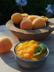 Homemade apricot jam with mint leaves in metal bowl. Apricots in wooden bowl on wooden table.