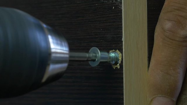 Man using an electric hand drill to drive a screw into a board. Dust motes shine in the air around. Tightening the screw, slow motion