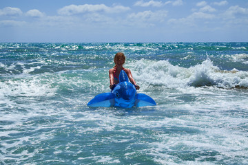 A girl riding an inflatable dolphin swims among the waves. Beach of Guardamar del Segura, Alicante....