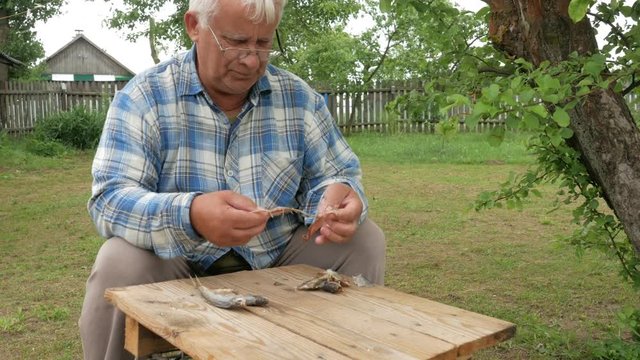 An elderly man is cleaning the dried fish in the garden on the table.