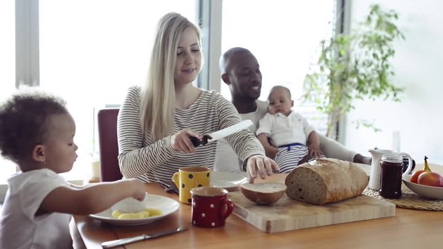 Young interracial family with little children having breakfast.