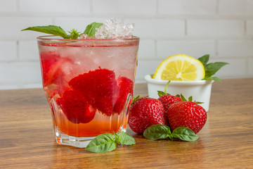 A refreshing summer drink with ice, strawberries and lemon on a wooden background. The concept of fruit drink.