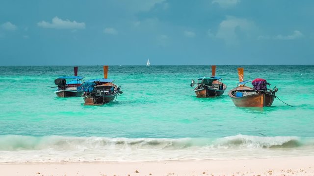Four long-tailed boat swinging in blue waves on Bundhaya beach, and white sail boat on the horizon, Koh Lipe Thailand
