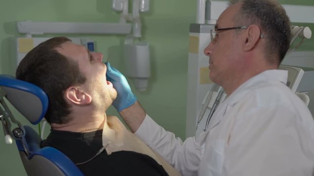 Dentist With a Mirror to Inspect the Oral Cavity of the Patient Sitting in the Dental Chair