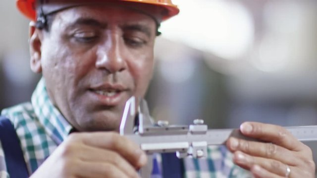 Closeup of factory worker in hardhat showing colleague how to use caliper